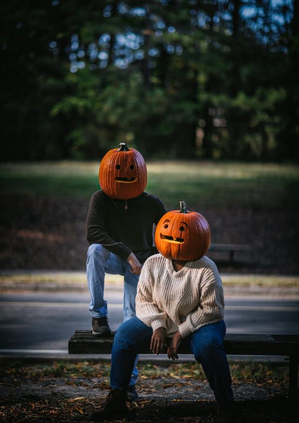 Two kids with pumpkin heads sitting on a bench